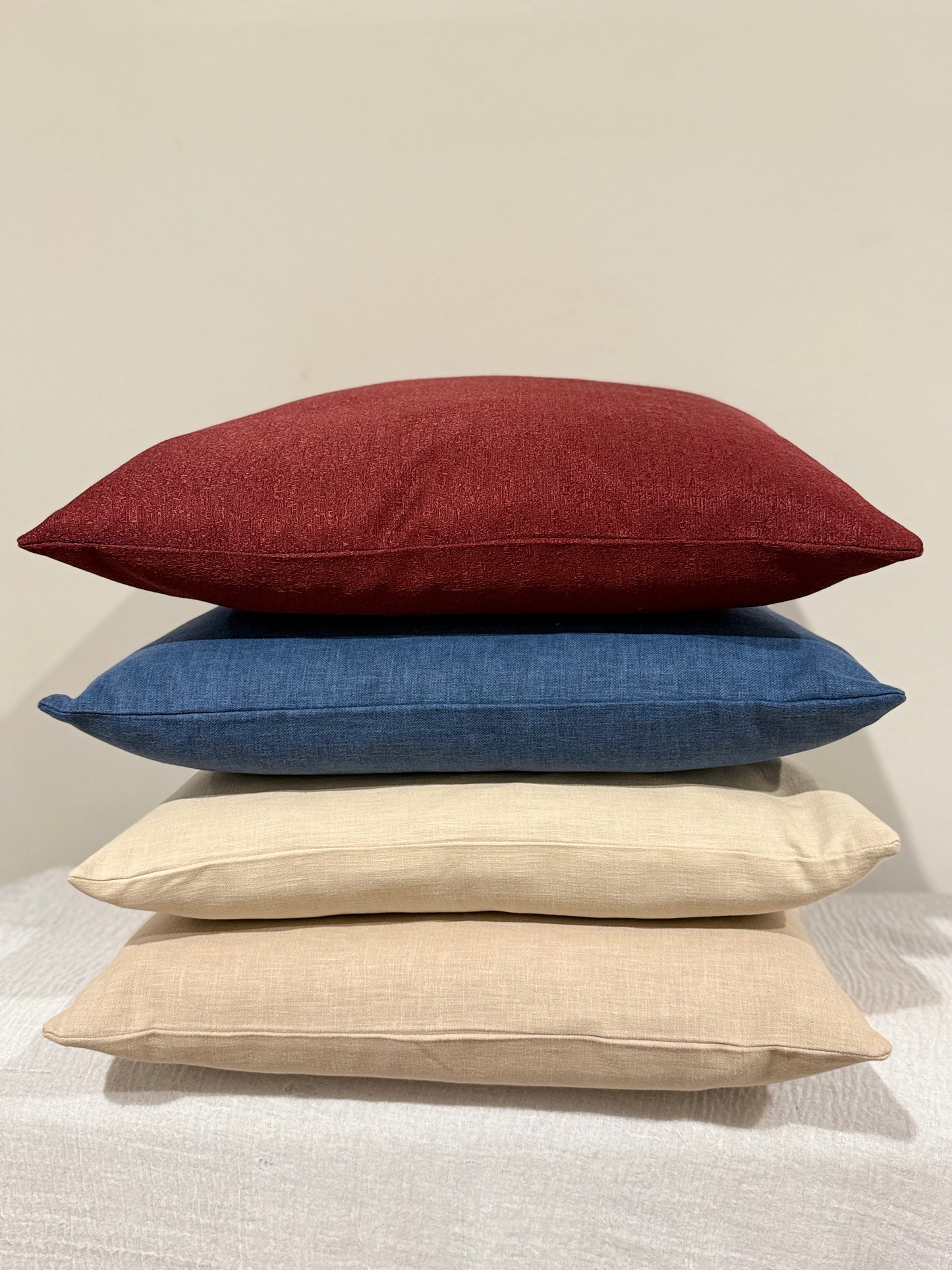 Stack of four cushions featuring Ruby Lux in red, Ink Blue, Stonewashed Beige, and Desert Sand, showcasing a mix of bold and neutral tones| interiors by zai