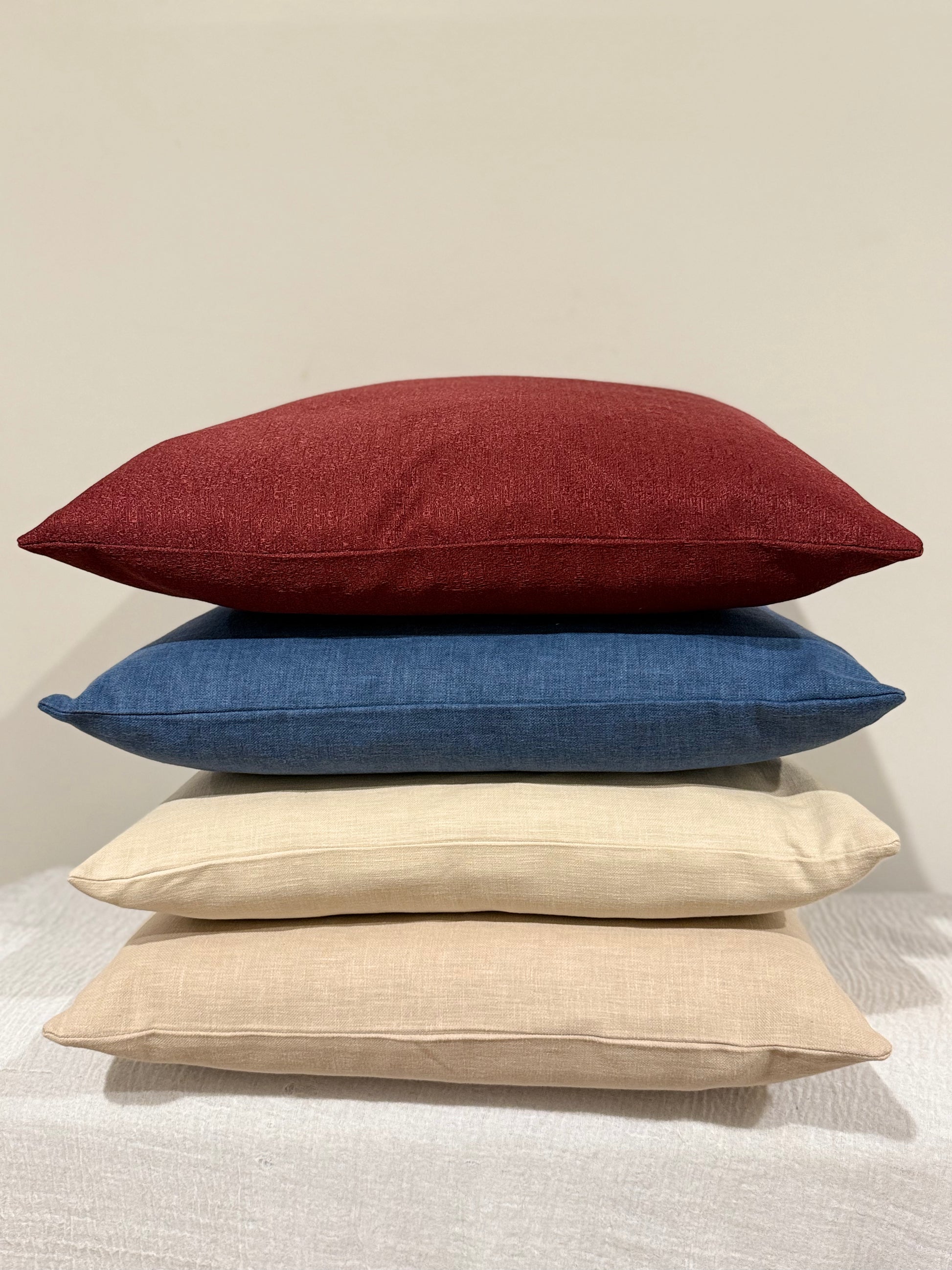 Stack of four cushions featuring Ruby Lux in red, Ink Blue, Stonewashed Beige, and Desert Sand, showcasing a mix of bold and neutral tones| interiors by zai